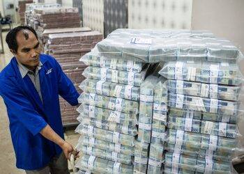 Petugas mendorong troli berisi tumpukan uang rupiah di Cash Center Bank Mandiri, Jakarta.